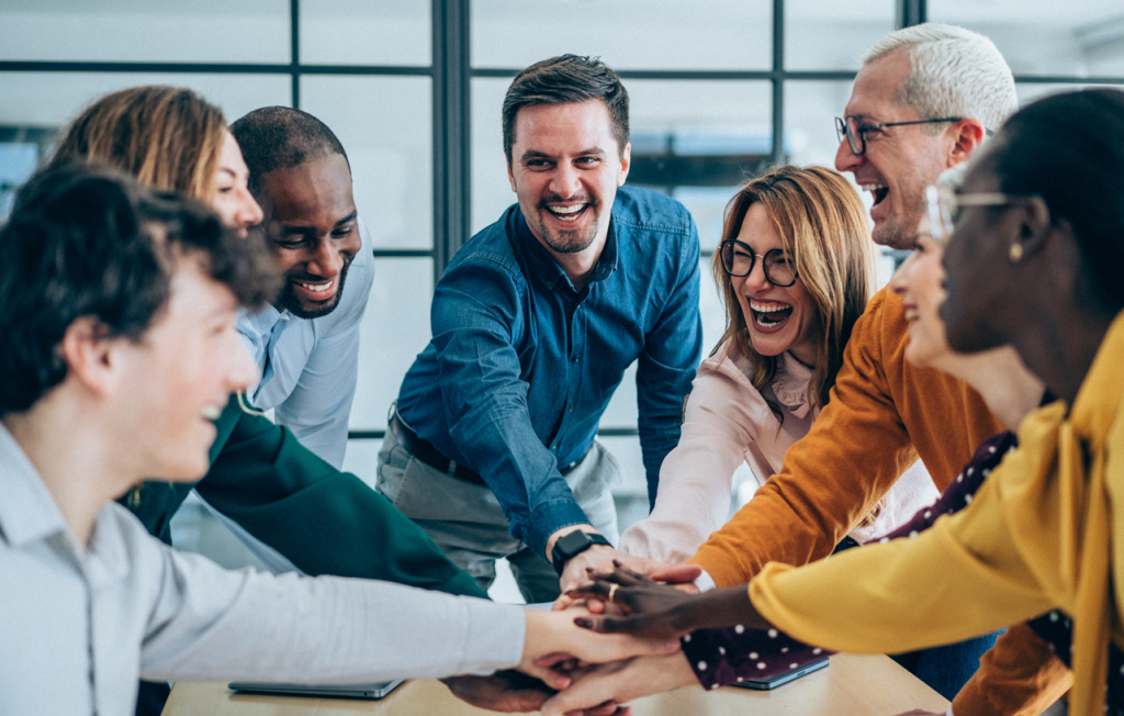 Aufnahme einer Gruppe von Menschen, die ihre Hände übereinanderlegen als Zeichen von Zusammenhalt und Teamwork. Lachende Lehrkräfte stapeln ihre Hände.