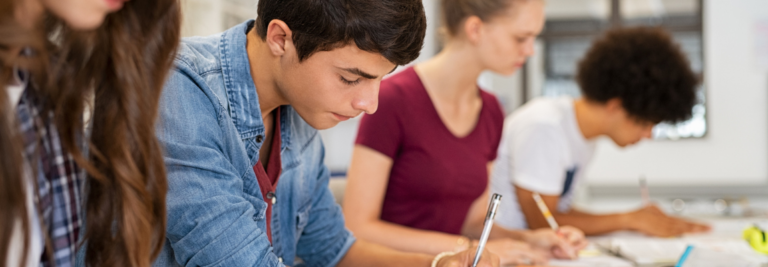 Schülerinnen und Schüler einer Berufsschule sitzen in der Schule und schreiben konzentriert in ihre Hefte.